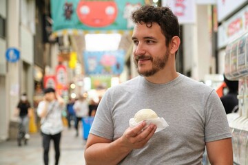 Latin young man tourist eating nikuman at Dotonbori street in Osaka, Japan.