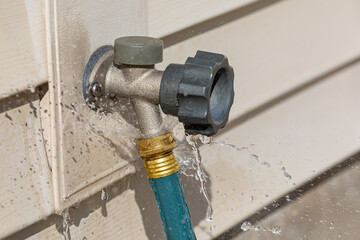 Water leaking from garden hose on outdoor spigot. Water waste, conservation and home repair concept.