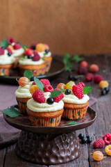 Cupcakes with butter cream and raspberry curd, decorated with berries on a wooden surface.
