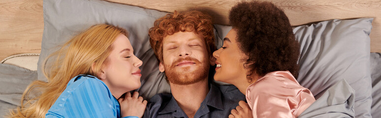 polyamory concept, man and interracial women in pajamas waking up together, morning, under blanket,...