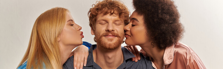 Obraz premium polygamy concept, open relationship, portrait of three adults, multicultural women kissing happy redhead man, polyamorous family in pajamas, cultural diversity, acceptance, banner
