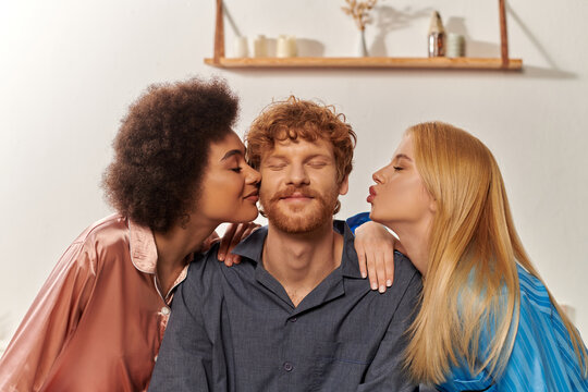 polygamy concept, open relationship, portrait of three adults, multicultural women kissing happy redhead man, polyamorous family in pajamas, cultural diversity, acceptance, bisexual, polyamory