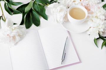 Morning coffee cup, diary and white peonies flowers on white table