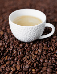 White cup of dark coffee on background from coffee beans