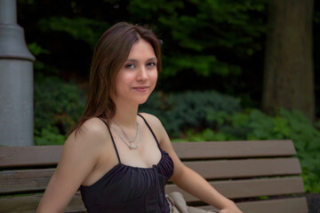 young female student sitting on a park bench in summer