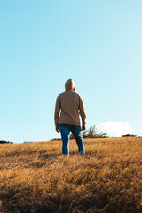 A young man back portrait with a cream hoodie in dry grass and blue sky background from golden hour sunset, puerto rico