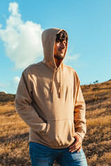 A young man portrait with a cream hoodie in dry grass and blue sky background from golden hour sunset, puerto rico