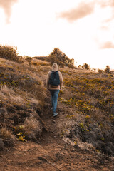 Fototapeta premium A man walking portrait carrying a dark blue bag pack on dry grass golden hour sunset from puerto rico