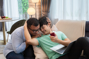 Asian LGBTQ+ making proposal by surprised gift wedding ring while partner lying down working at home, happy homosexual gay fall in love live together at home spend time building a family relationship