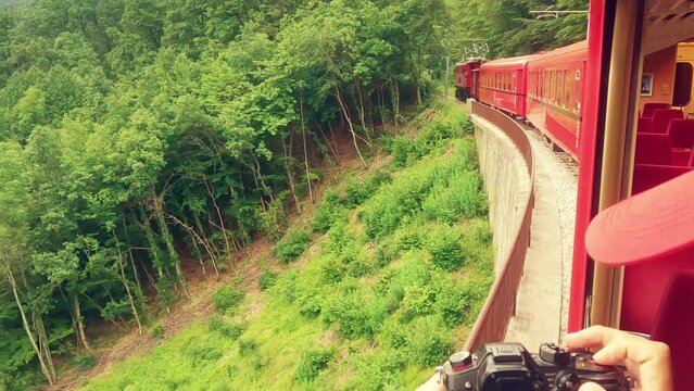 Photographer wearing red cap takes pictures of a retro red train in beautiful scenery