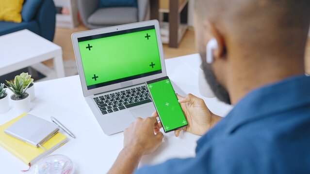 African American man using smartphone and laptop with pre-keyed green screen to order services online