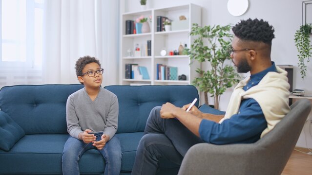 School psychologist communicating with a boy and taking notes, child counselling
