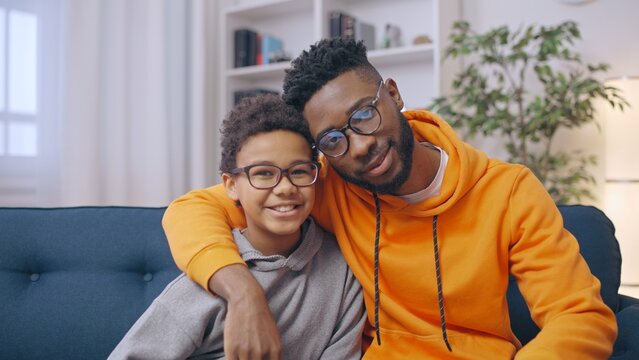 Portrait of African American brothers hugging on sofa at home, happy siblings