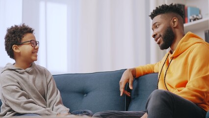 African American father and little son having conversation on couch, spending time together