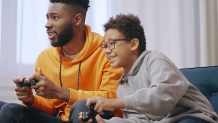 Obraz premium Cheerful African American brothers playing video games while sitting on couch at home