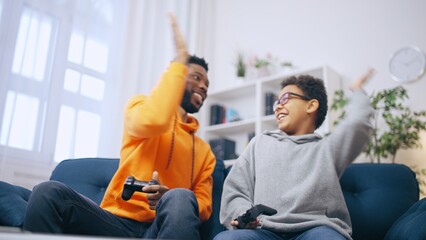 Cheerful elder and younger brother giving each other high five after victory in a video game