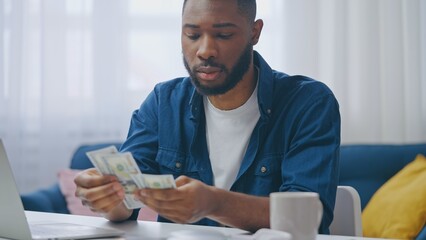 African American man counting money, satisfied with salary, saving for a dream