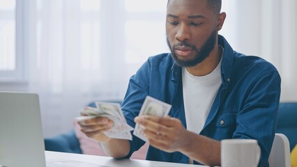 Upset African American man counting money, unhappy with low income and his finances