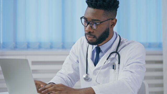 African American doctor typing on laptop, working on patient's medical records