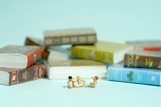 Miniature tiny people toy figure photography. Read concept. Group of infant toddlers sitting in front of story book pile. Isolated on blue background
