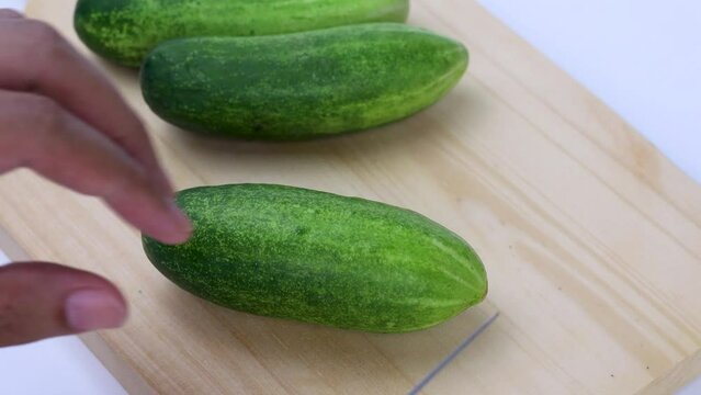 hand slicing cucumber on wooden cutting board
