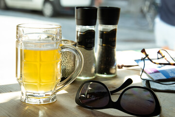 Mug of beer and sunglasses on the table in the restaurant