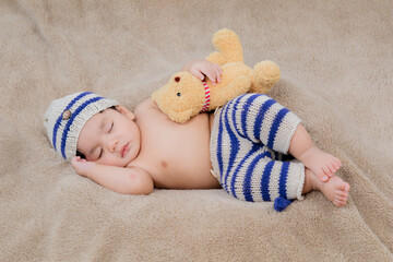 Asian Newborn baby wearing blue knit hat and pants deeply sleeping with teddy bear on brown bed at...