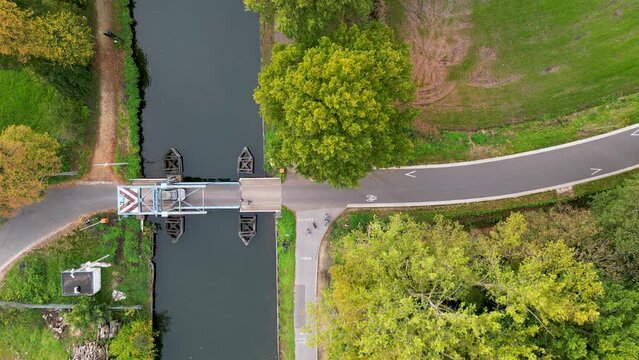 Engaging aerial top-down footage showing traffic in motion as it crosses a quaint draw bridge over a peaceful countryside canal. The blend of rural charm and modern mobility brings to life the