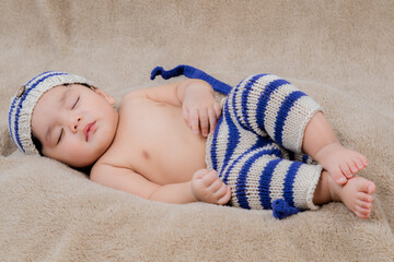 Asian Newborn baby wearing blue knit hat and pants deeply sleeping with teddy bear on brown bed at...
