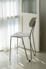 white chair on a shiny floor in front of windows with white curtains.