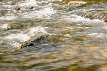 Rapid and powerful water flow between large rocks, close-up. Boulders in cold mountain river. Natural backgrounds
