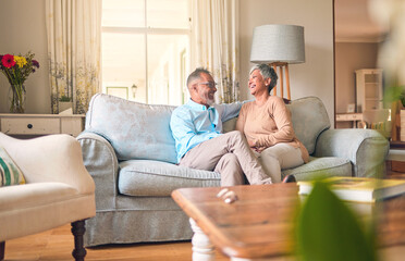Couch, love and senior couple relax and laugh together in a home for a conversation and bonding on retirement. Elderly man and woman in a living room for happiness, joke and happy in a marriage