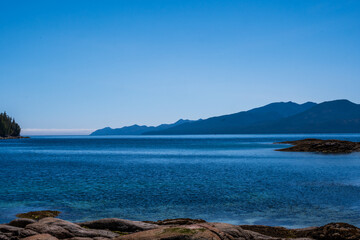 Fototapeta na wymiar sea sky and mountains with rocky beach foreground shot in fitz hugh sound, british columbia