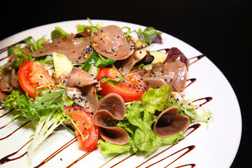 Salad with beef tongue with vegetables and herbs, dressed with sauce on a white plate.