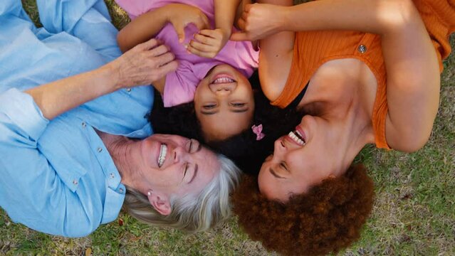 Overhead portrait shot of multi-generation female family lying on grass together tickling granddaughter - shot in slow motion