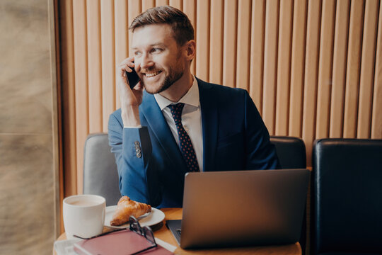 Bearded businessman chatting, laptop on table, coffee break, remote work.