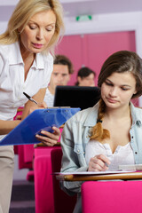 teacher stood by university student making notes on clipboard