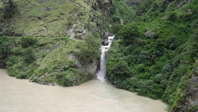 Waterfall cascades over a white-water river that originates from glaciers amidst the forest.