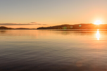 Sunset over a lake with forested shores at the peak of fall foliage. Lens flare.