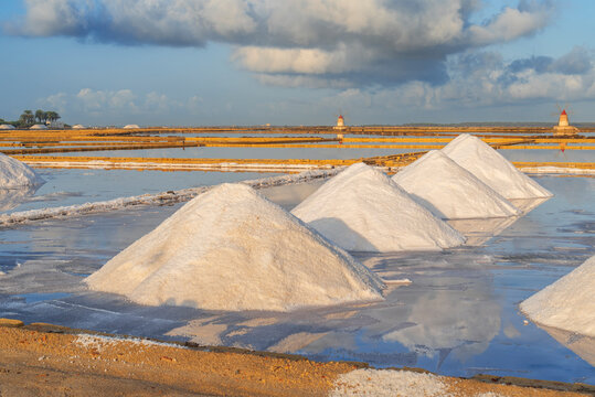 Piles of salts among salt flats with windmills in the background at sunset, Saline Ettore e Infersa, Marsala, province of Trapani, Sicily