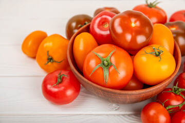 Tomatoes on a white wooden background. Cherry tomatoes, yellow, pink, brown and black tomatoes in a bowl. Organic vegetables, harvesting.Vegan. Fresh ripe tomatoes. copy space.