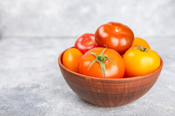 Tomatoes on marble texture background. Cherry tomatoes, yellow, pink, brown and black tomatoes in a bowl. Organic vegetables, harvesting.Vegan. Fresh ripe tomatoes. copy space.