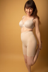 Studio portrait of a caucasian woman in her 30s wearing nude colour shapewear and a bra. The studio...