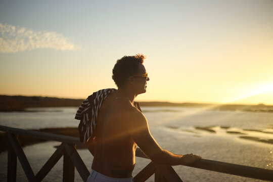 Um momento de contempla&ccedil;&atilde;o: um belo homem bronzeado aprecia o p&ocirc;r do sol sobre o passadi&ccedil;o da Ria Formosa, no Algarve, durante o ver&atilde;o em Portugal, desfrutando da tranquilidade e da beleza da paisagem