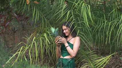 young woman is looking at an exotic fruit against the backdrop of bushes