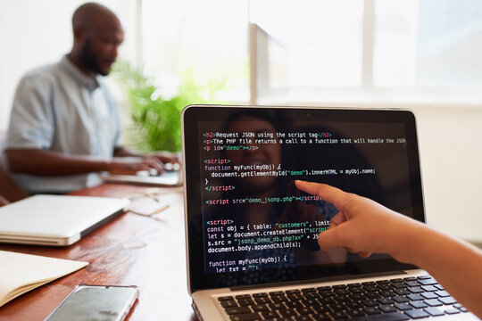 Young female developer points finger to laptop screen with javascript code 