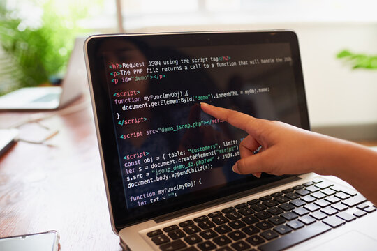 Young female developer points finger to laptop screen with javascript code 