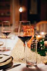 Close up of glass with red wine on festively decorated christmas dinner table.
