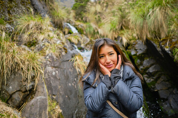 brown-skinned latina woman smiling and touching her face with her hands next to a waterfall in the...