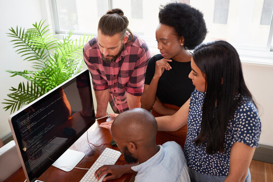 Overhead shot of four developers working together, reviewing code on big screen